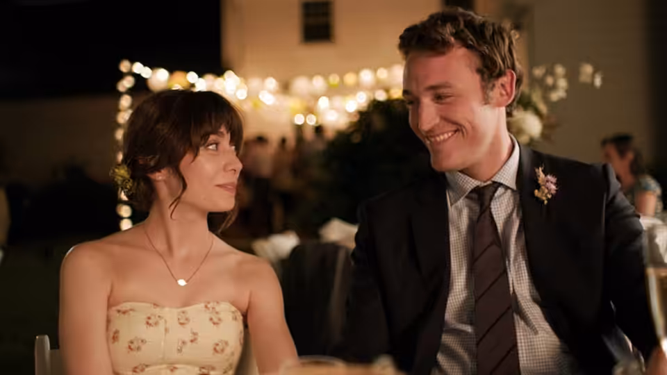 Sonia Friedman (Cristin Milioti) and a suited man sit together at a warmly lit wedding reception