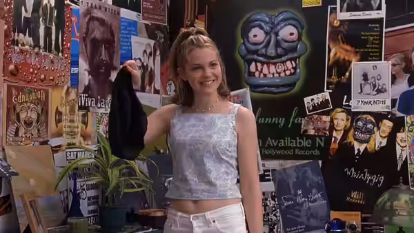 Katarina Stratford (Julia Stiles) smiles while holding a black garment in her poster-covered room