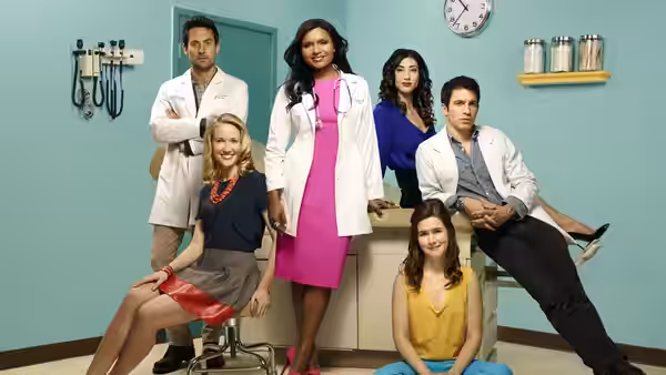 Dr. Mindy Lahiri (Mindy Kaling) stands among colleagues in a clinic, with doctors seated around her