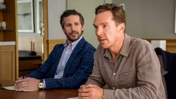 Theo Rose (Benedict Cumberbatch) leans forward at a table beside a bearded man