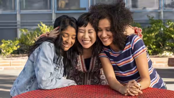Devi, Eleanor, and Fabiola lean together around an outdoor table