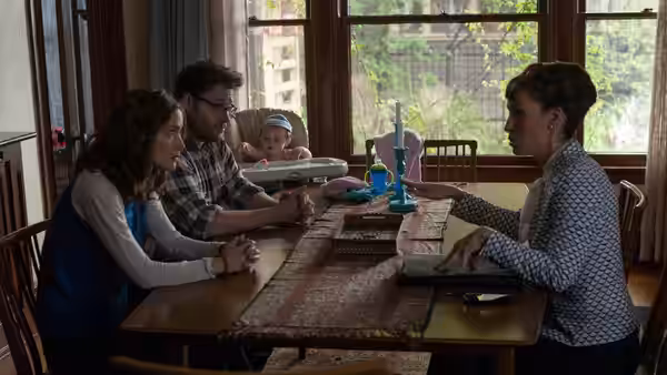 Mac and Kelly sit with their baby across the dining table from a woman