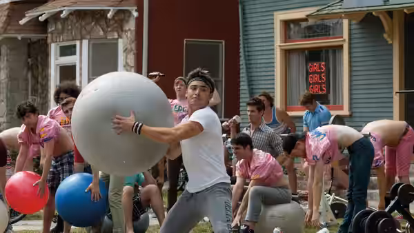 Teddy holds a large ball as fraternity brothers gather outside their house