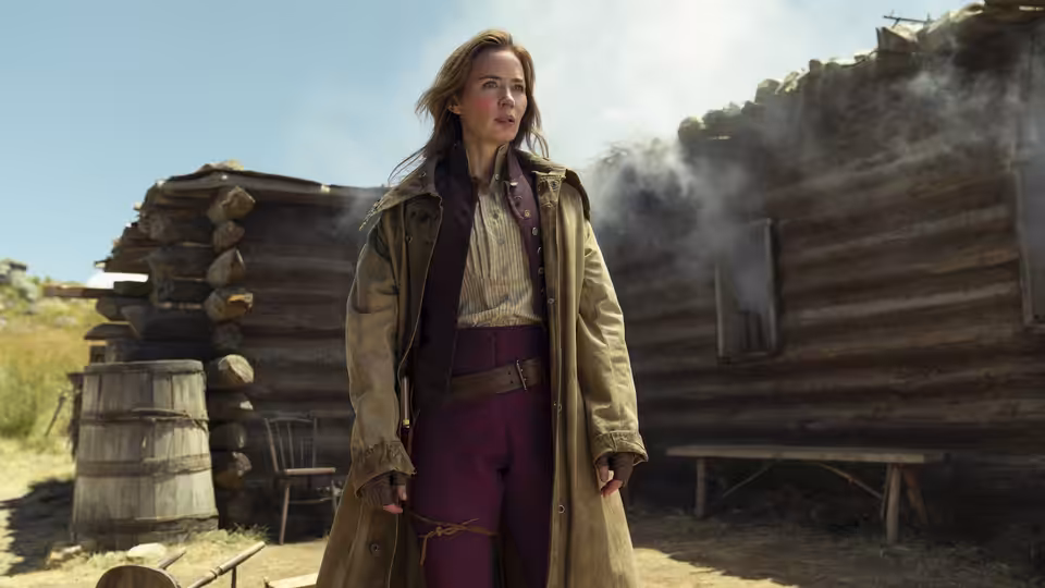 Lady Cornelia Locke (Emily Blunt) stands outside a smoking log cabin in the countryside