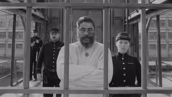 Moses Rosenthaler (Benicio del Toro), wrapped in a white robe, stands behind prison bars with guards
