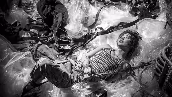 A bound woman lies among plastic sheeting and rubbish