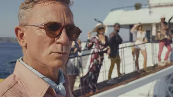 Benoit Blanc (Daniel Craig) stands by a yacht as guests gather on the gangway