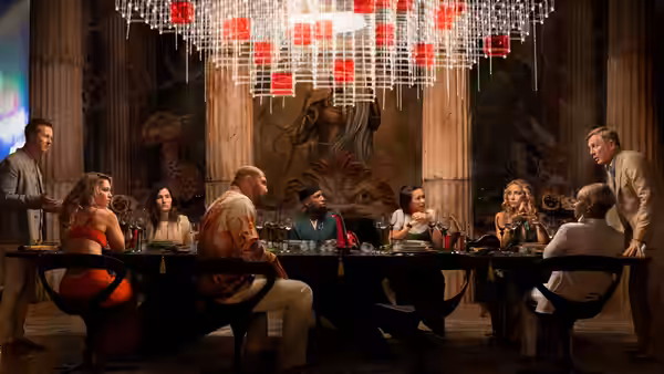 Benoit Blanc (Daniel Craig) and the guests gather around a long table beneath a chandelier