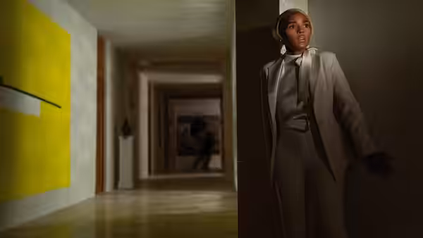 Andi Brand (Janelle Monáe) peeks around a doorway into a dim hallway