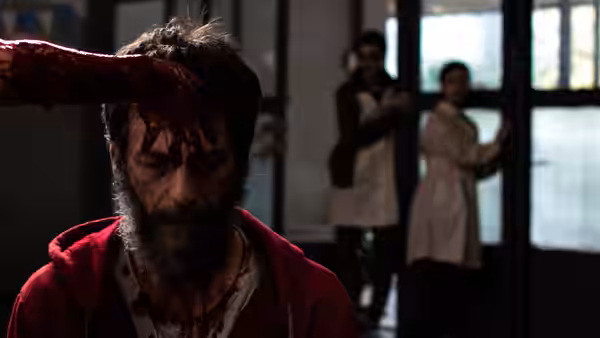 Pedro (Ezequiel Rodríguez), bloodied in a red jacket, stands before two women at a doorway
