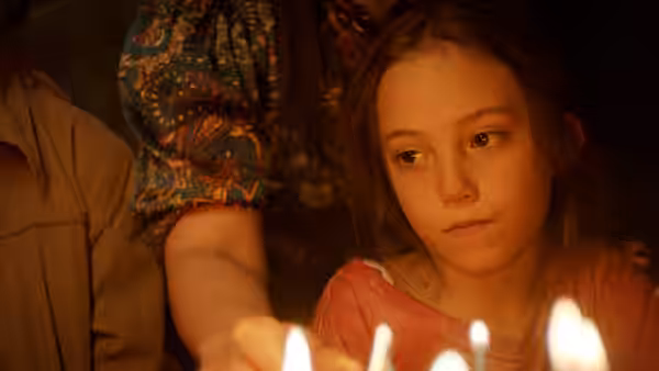 Sol (Naíma Sentíes) watches candle flames beside an adult in a colorful shirt