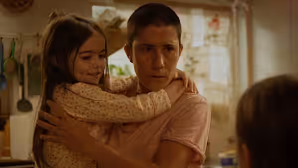 A woman carries a smiling girl in her arms in a sunlit kitchen