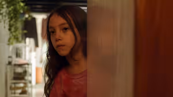 Sol (Naíma Sentíes) peers around a doorway into a bright room