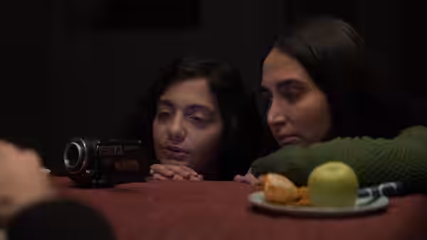 Two young women peer over a table beside a camcorder and a plate of fruit