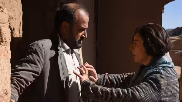 A woman presses her hands against a bearded man's chest in a stone doorway