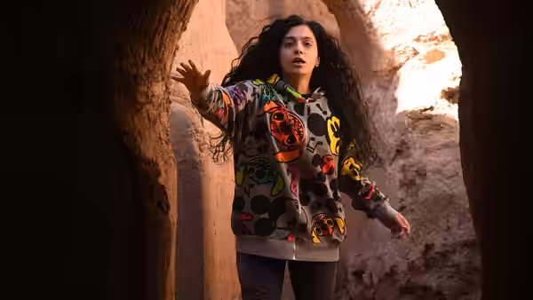 A young woman in a colorful hoodie reaches through a narrow stone passage