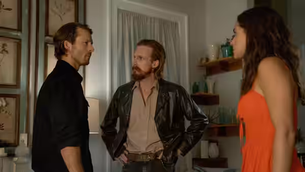 Gary Johnson (Glen Powell), a bearded man, and Madison Figueroa Masters (Adria Arjona) face each other indoors