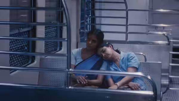 Prabha and Anu rest together on a metal bench inside a train carriage
