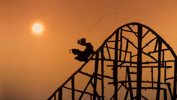 A silhouetted rider climbs a roller coaster against the setting sun