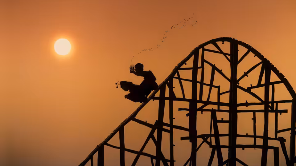 A silhouetted rider climbs a roller coaster against the setting sun
