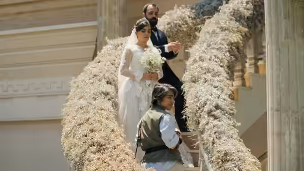 A bride holding flowers and a young girl stand among towering white wedding decorations