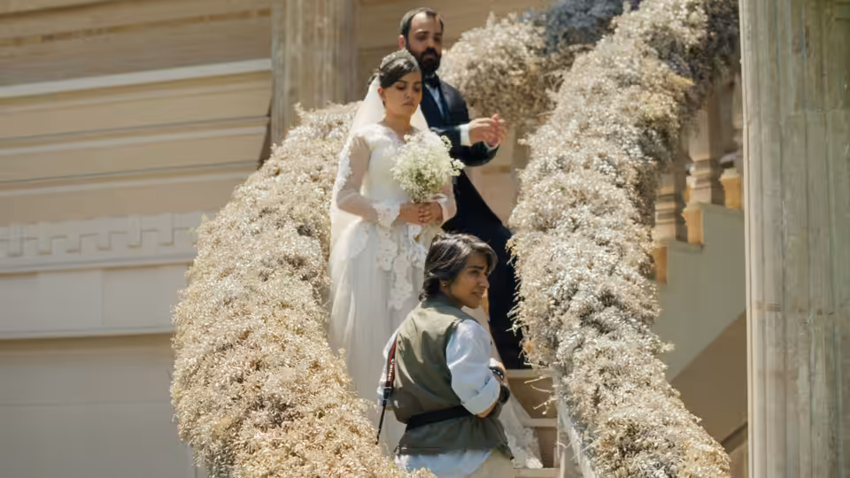 A bride holding flowers and a young girl stand among towering white wedding decorations