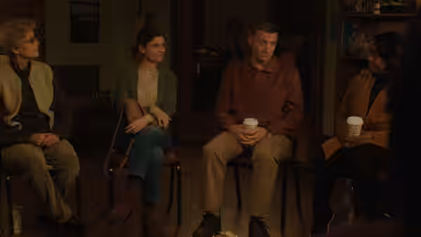 Craig Waterman (Tim Robinson) sits with a group of people holding a cup