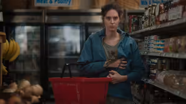 Agnes (Eva Victor) shops in a grocery store, holding her stomach beside a red basket