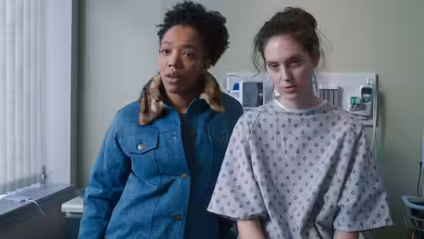 Lydie (Naomi Ackie) stands beside Agnes (Eva Victor) in a hospital gown