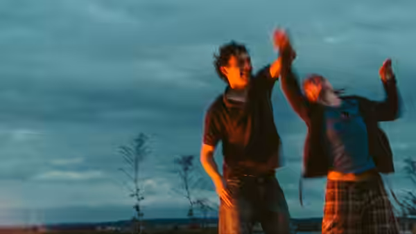 A man and woman dance together outdoors beneath a cloudy sky