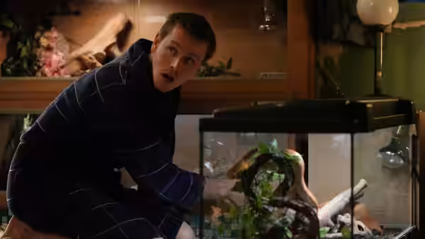 A man crouches beside an aquarium in a wood-paneled room