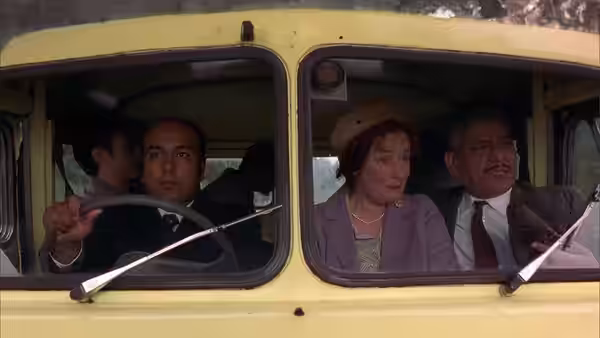 A man drives a yellow van while a woman and man sit beside him
