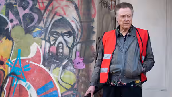 Frank (Christopher Walken) stands beside a graffiti-covered wall in a red reflective vest