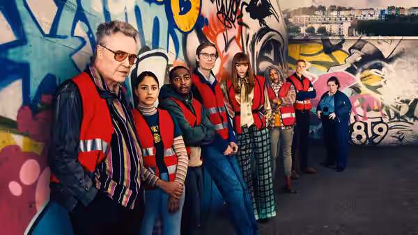 Frank and fellow volunteers line a graffiti-covered wall in red work vests