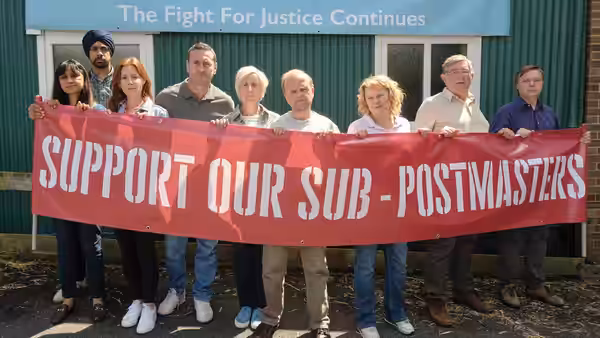 Post Office campaigners hold a banner supporting sub-postmasters outside a green-clad building