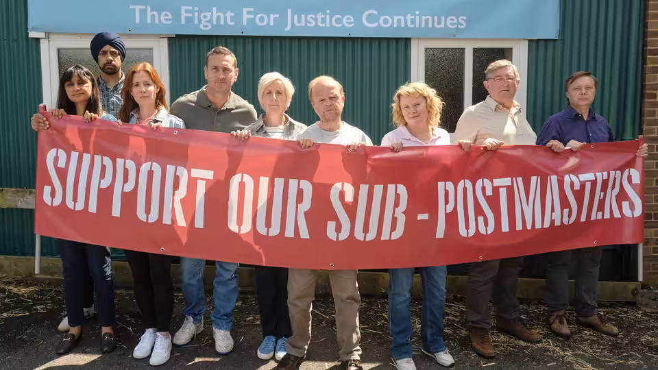 Post Office campaigners hold a banner supporting sub-postmasters outside a green-clad building