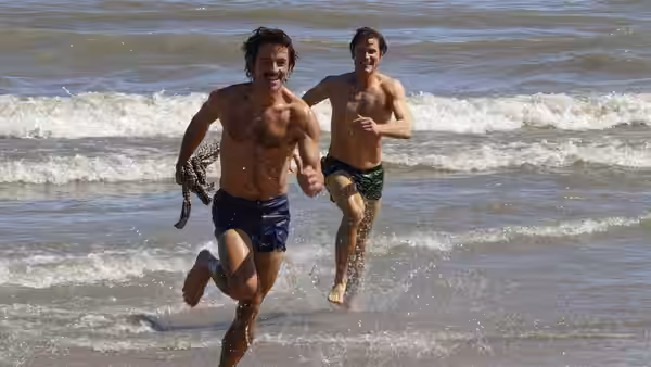Hawk Fuller (Matt Bomer) and Tim Laughlin (Jonathan Bailey) run from the surf