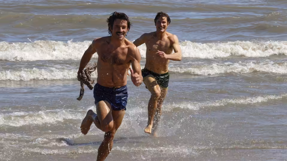 Hawk Fuller (Matt Bomer) and Tim Laughlin (Jonathan Bailey) run from the surf