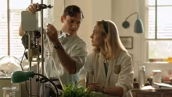 Calvin Evans (Lewis Pullman) demonstrates laboratory equipment beside Elizabeth Zott (Brie Larson)
