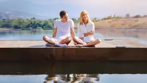 Calvin Evans and Elizabeth Zott sit together on a dock beside the water