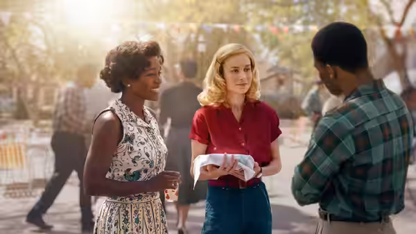 Elizabeth Zott and Harriet Sloane speak with a man outdoors among picnic tables
