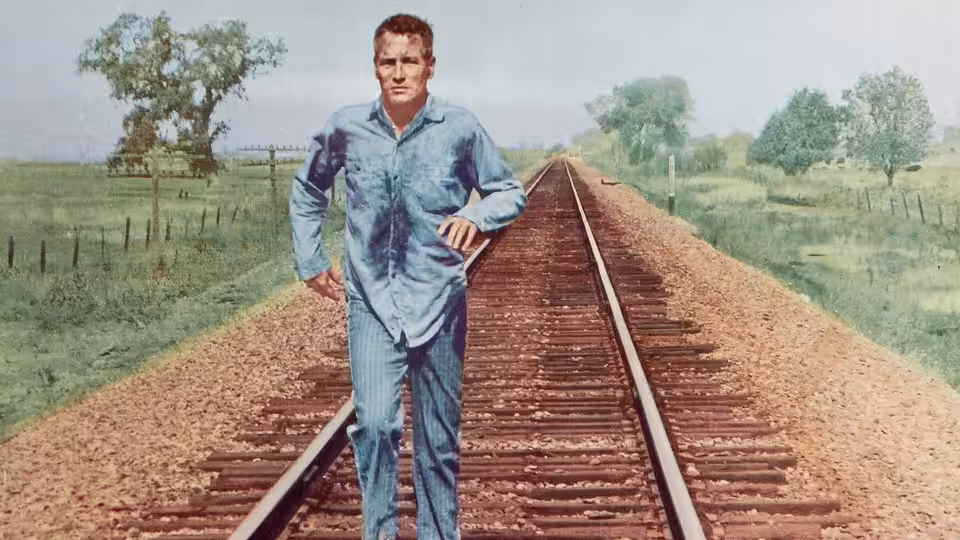 Luke Jackson (Paul Newman) walks along railway tracks in his prison work clothes