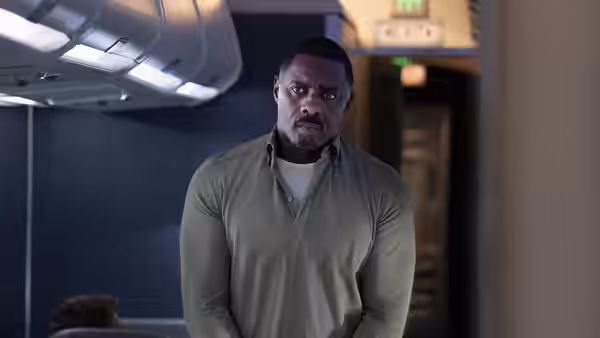 Sam Nelson (Idris Elba) stands in the airplane aisle beneath the overhead bins