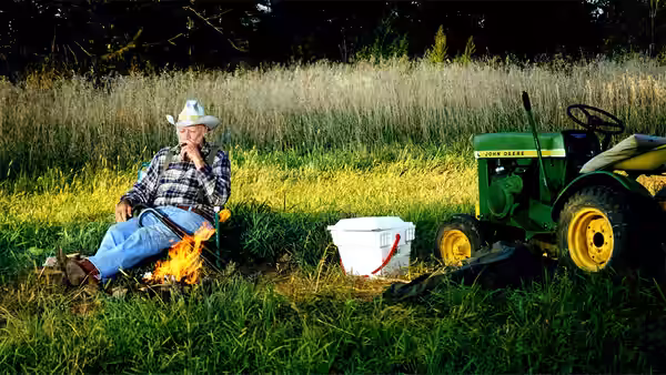 Alvin (Richard Farnsworth) seated by a small fire beside his tractor in a field
