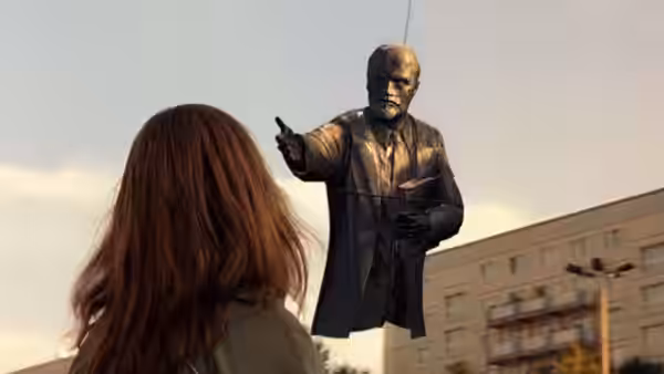 A woman with long hair watching a Lenin statue being lifted by crane