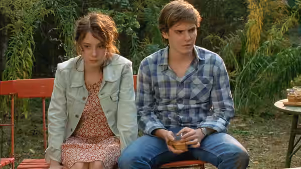 Alex (Daniel Brühl) sitting on a bench with a young woman outdoors