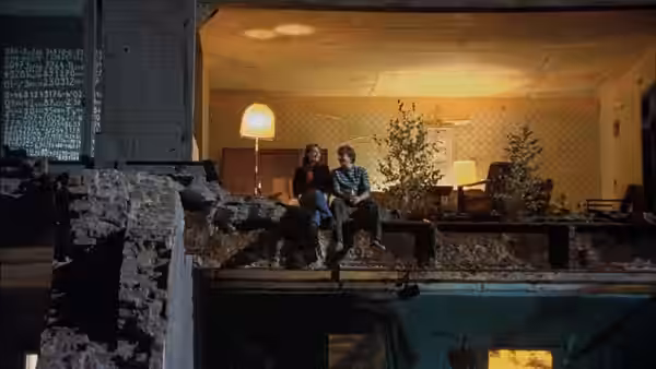 Alex (Daniel Brühl) and a woman sitting on a ledge inside a ruined building