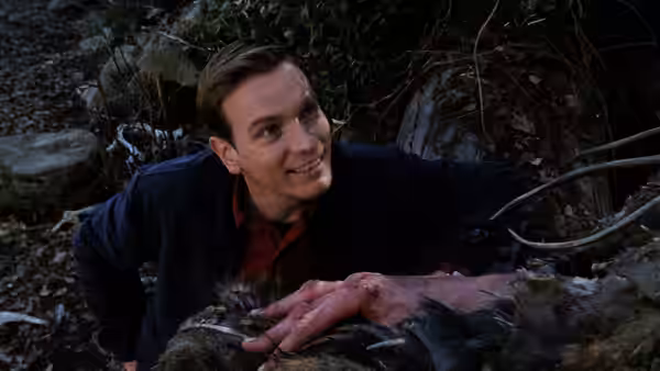 Young Ed Bloom lies smiling in the woods with his hand on dark fur