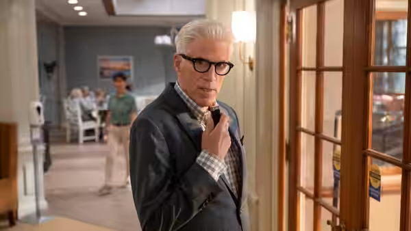 Charles Nieuwendyk (Ted Danson) adjusts his tie beside a doorway in a care facility