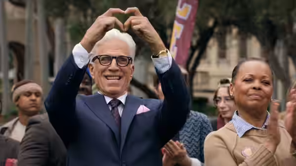 Charles Nieuwendyk (Ted Danson) makes a heart shape with his hands among applauding people outdoors